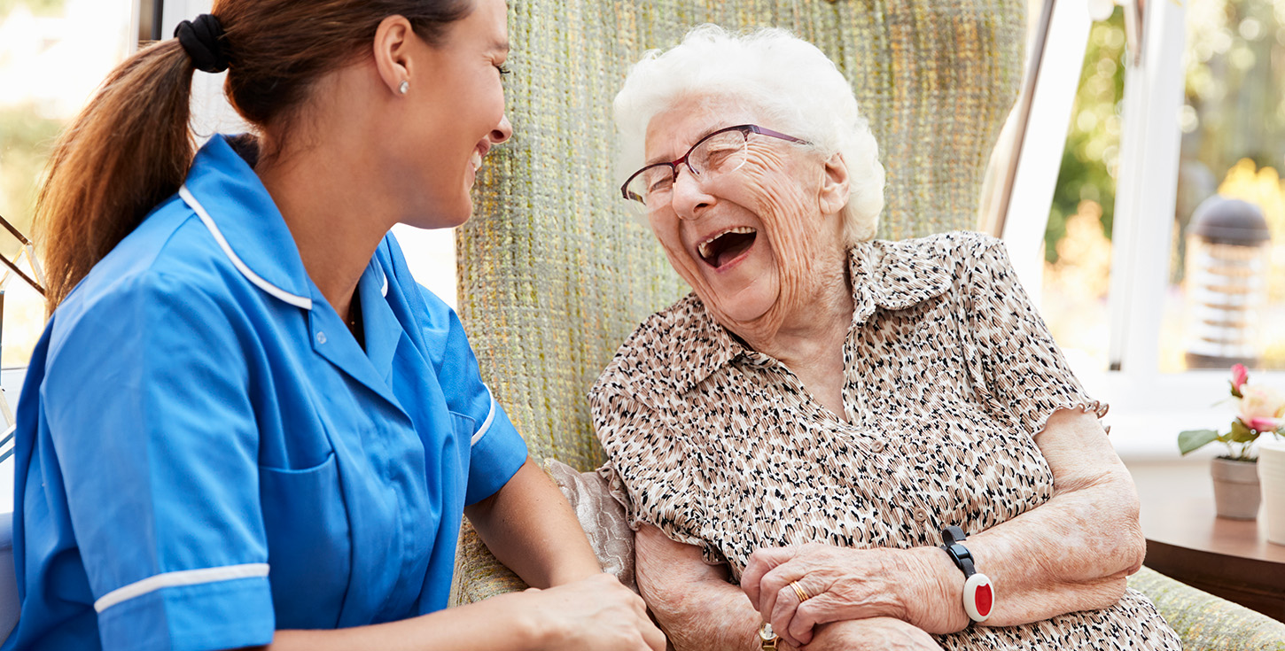 Senior Woman Sitting In Chair And Laughing With Nurse