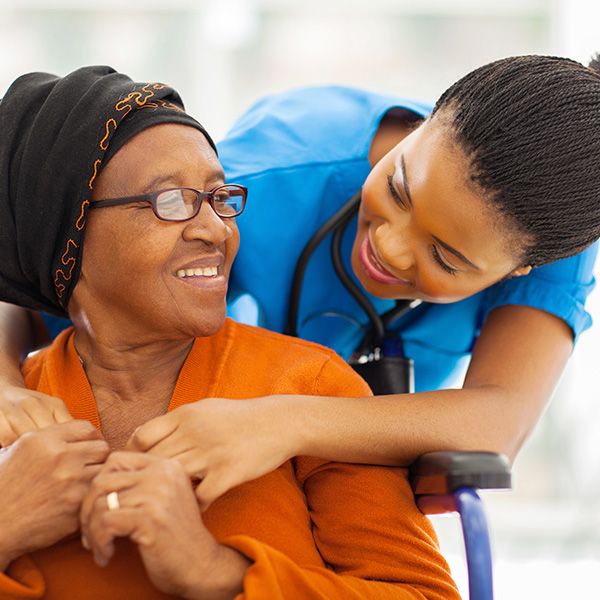 black female nurse hugging black senior woman in wheelchair