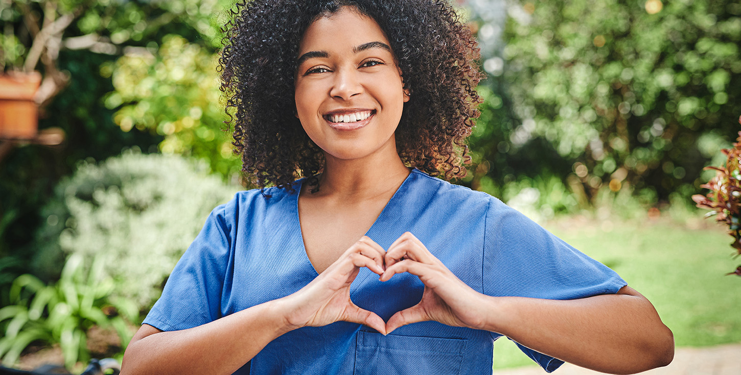 young nurse standing alone outside and making heart shaped gesture