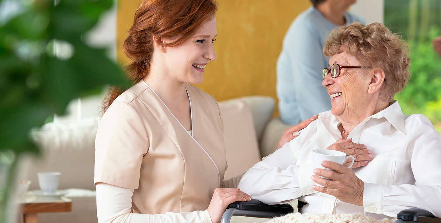 young smiling nurse helping comforting elderly woman in wheelchair